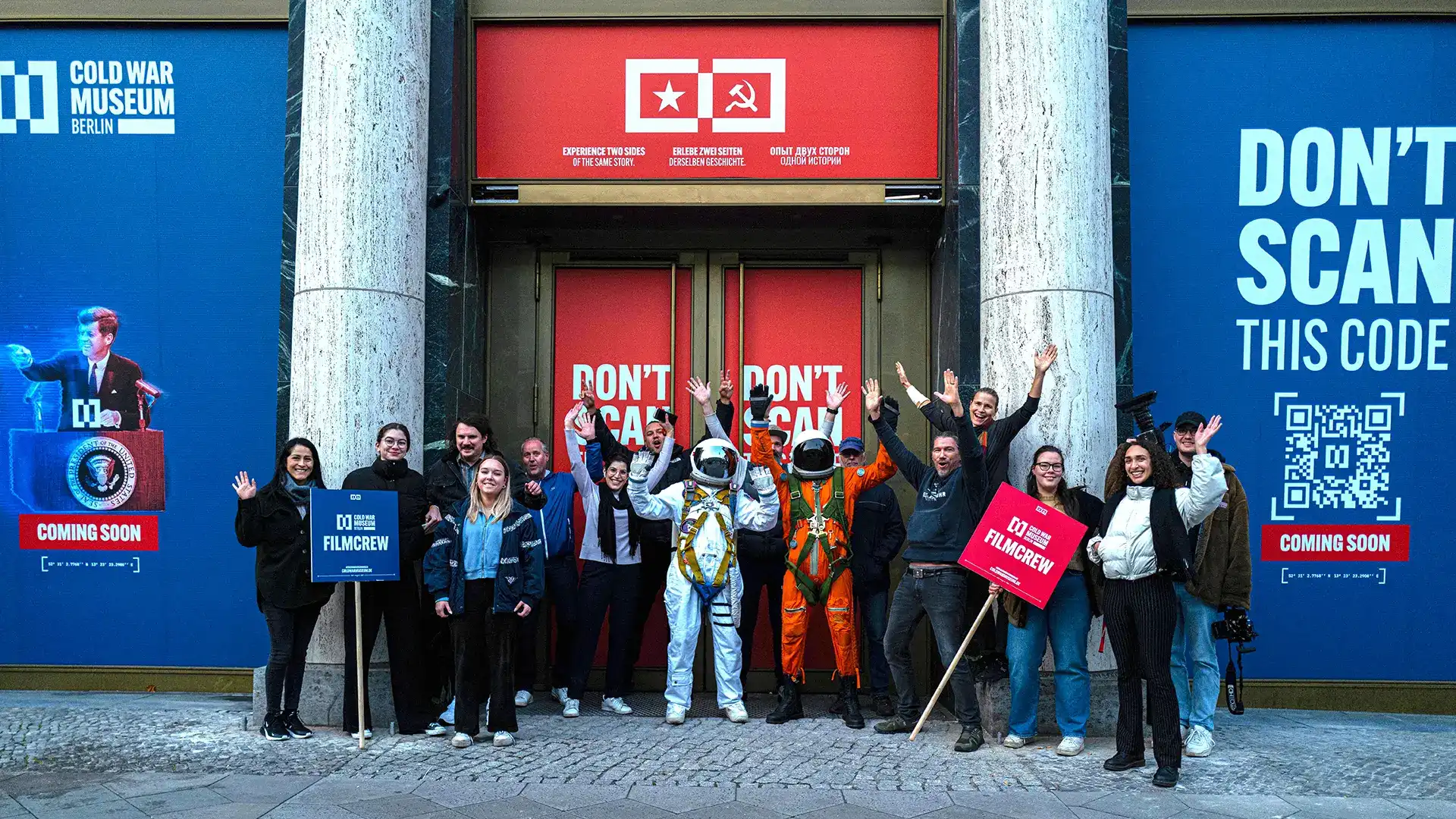 Ein Bild zeigt das Team des Cold War Museums beim Jubeln vor dem Cold War Museum Berlin.