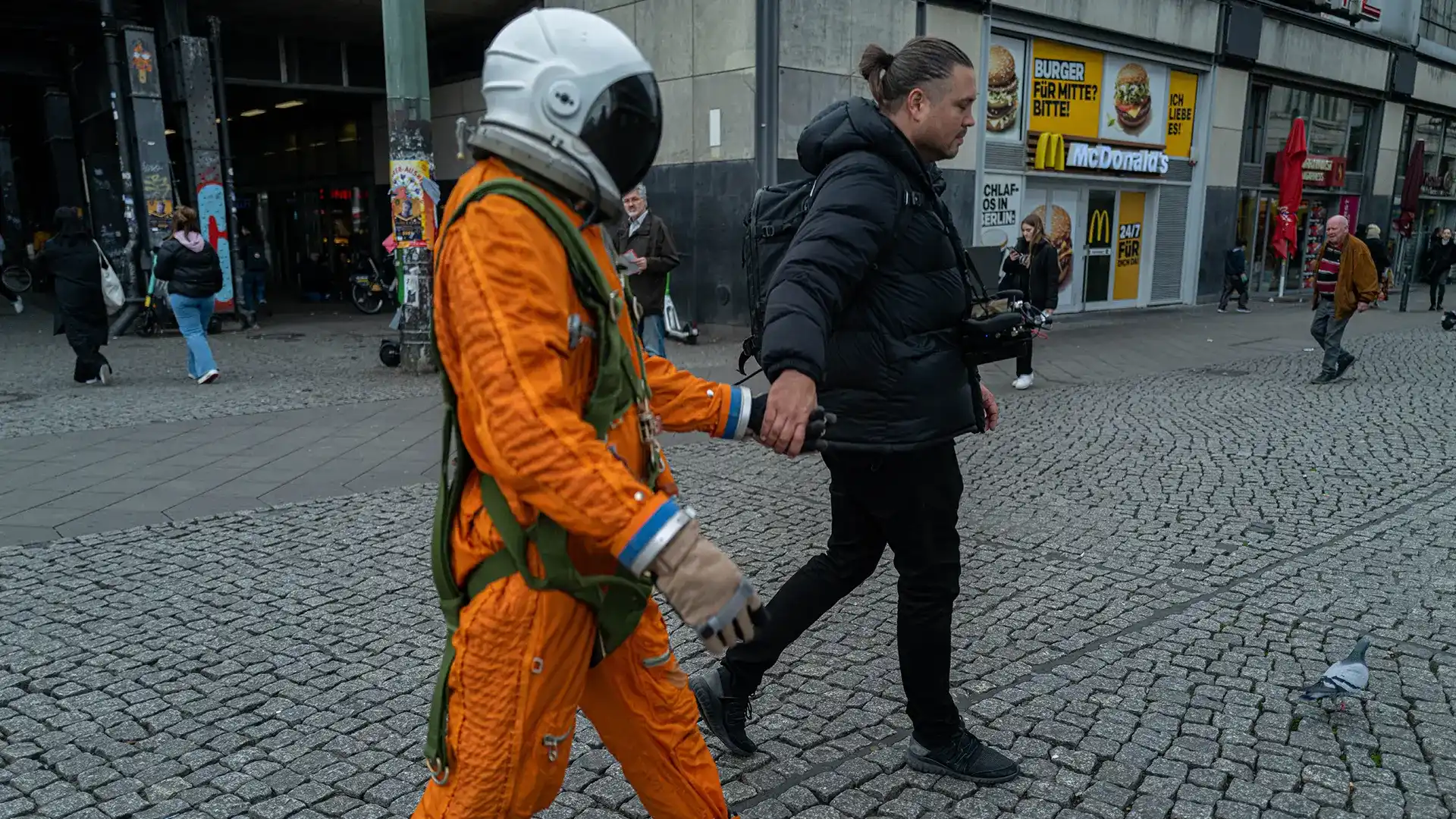 Ein Bild zeigt einen Astronauten Hand in Hand mit einem anderen Mann der schwarz gekleidet ist.